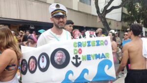 Fantasia sobre o cruzeiro do Neymar. Homem com roupa de marinheiro segurando um cartaz escrito: cruzeiro do Neymar,